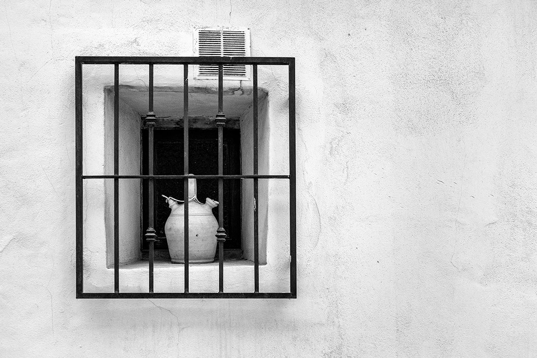 A jug on the sill of a barred window.